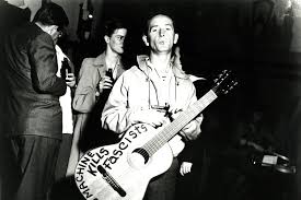 woody-guthrie-with-guitar-this-machine-kills-fascists.jpg